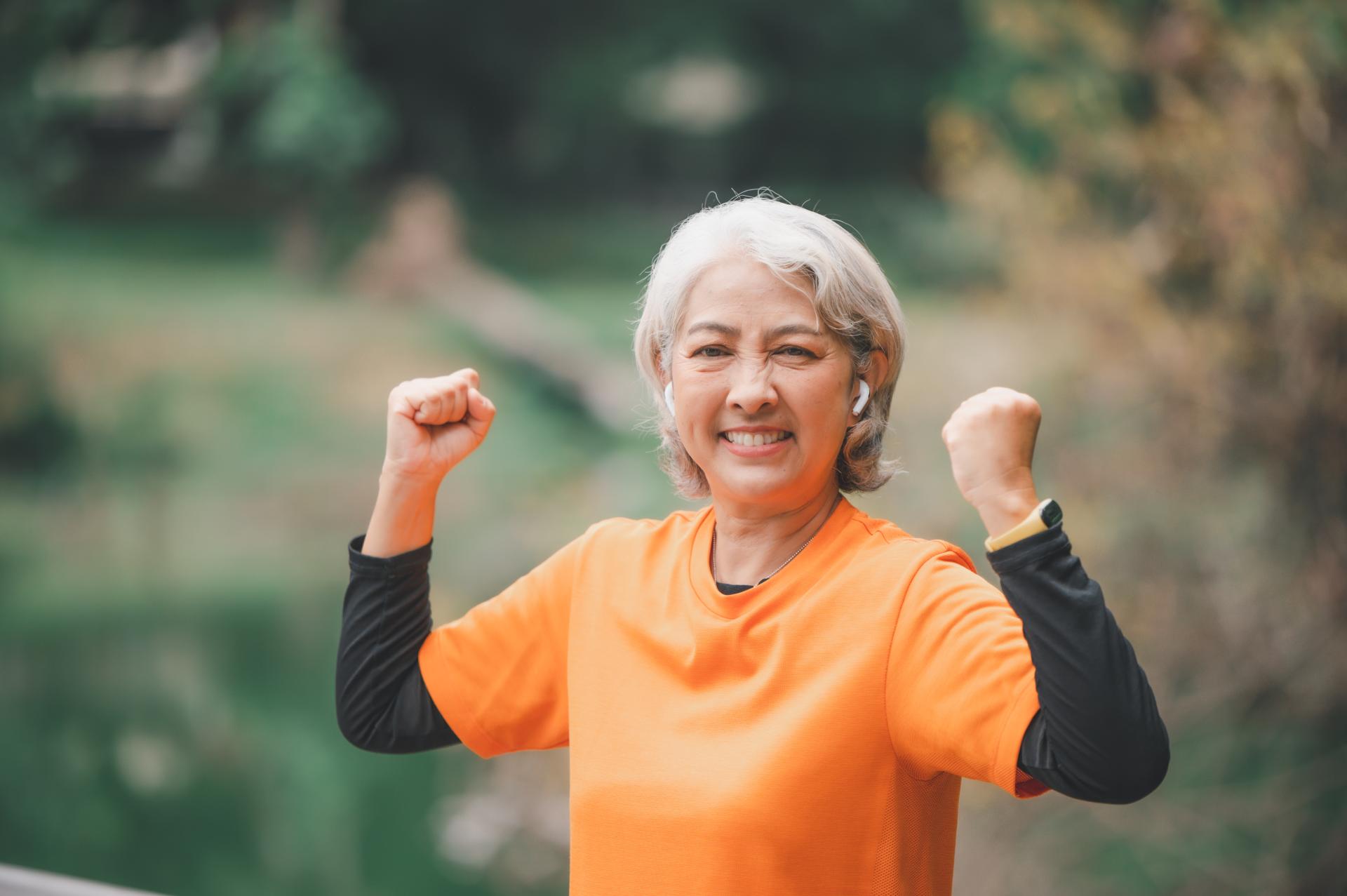 Active senior woman smiling and flexing arms outdoors.