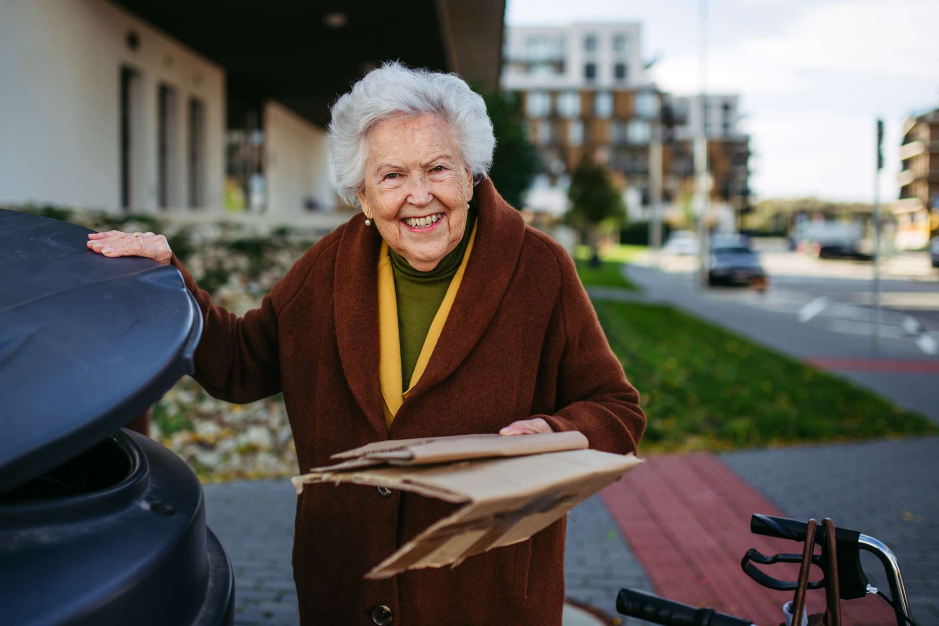 An elderly woman showing indepence in throwing cardboards in the trash bin.