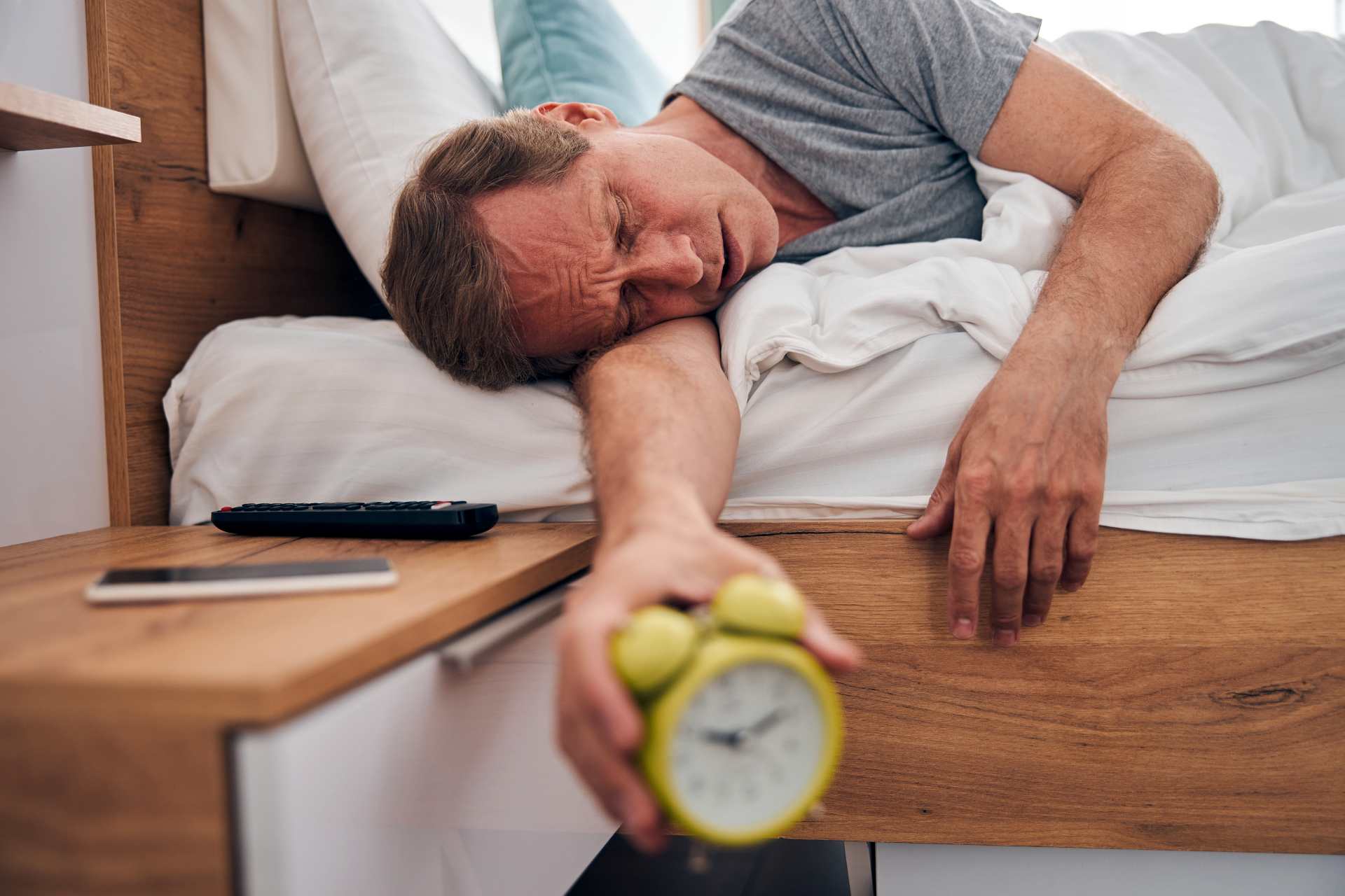 Tired man reaching to turn off an alarm clock in bed.