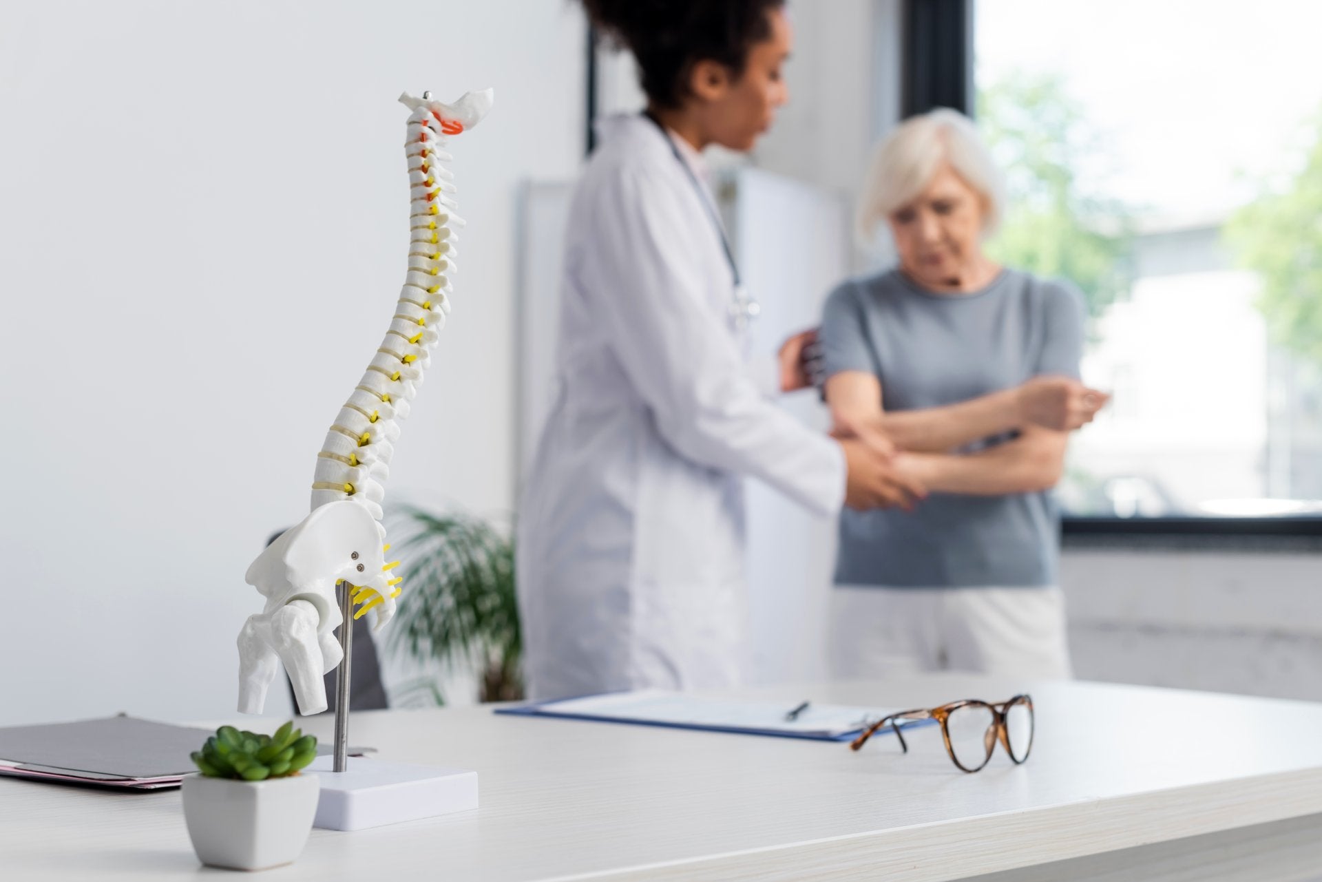 Senior woman consulting with a healthcare provider about osteoporosis prevention, with a spinal model representing bone strength and posture.