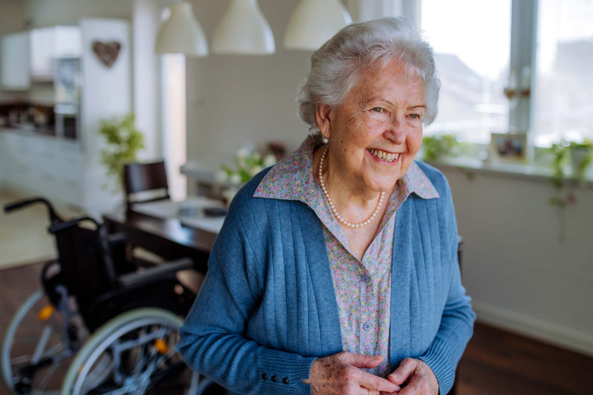 Smiling senior woman standing confidently in her home with a wheelchair nearby, representing independence, safety, and successful aging in place.