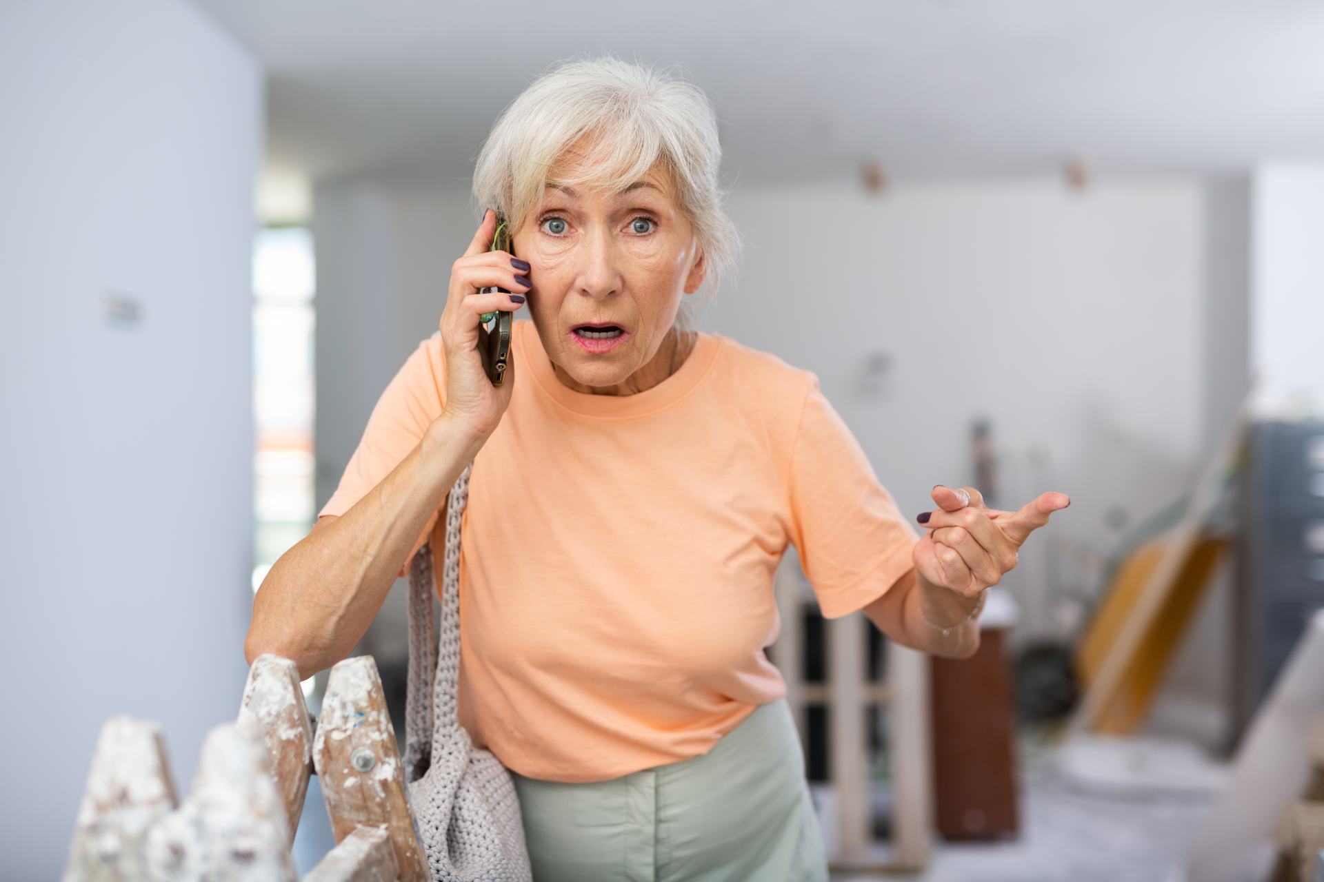 Senior woman looking surprised while answering a phone call at home, illustrating common scam call scenarios.